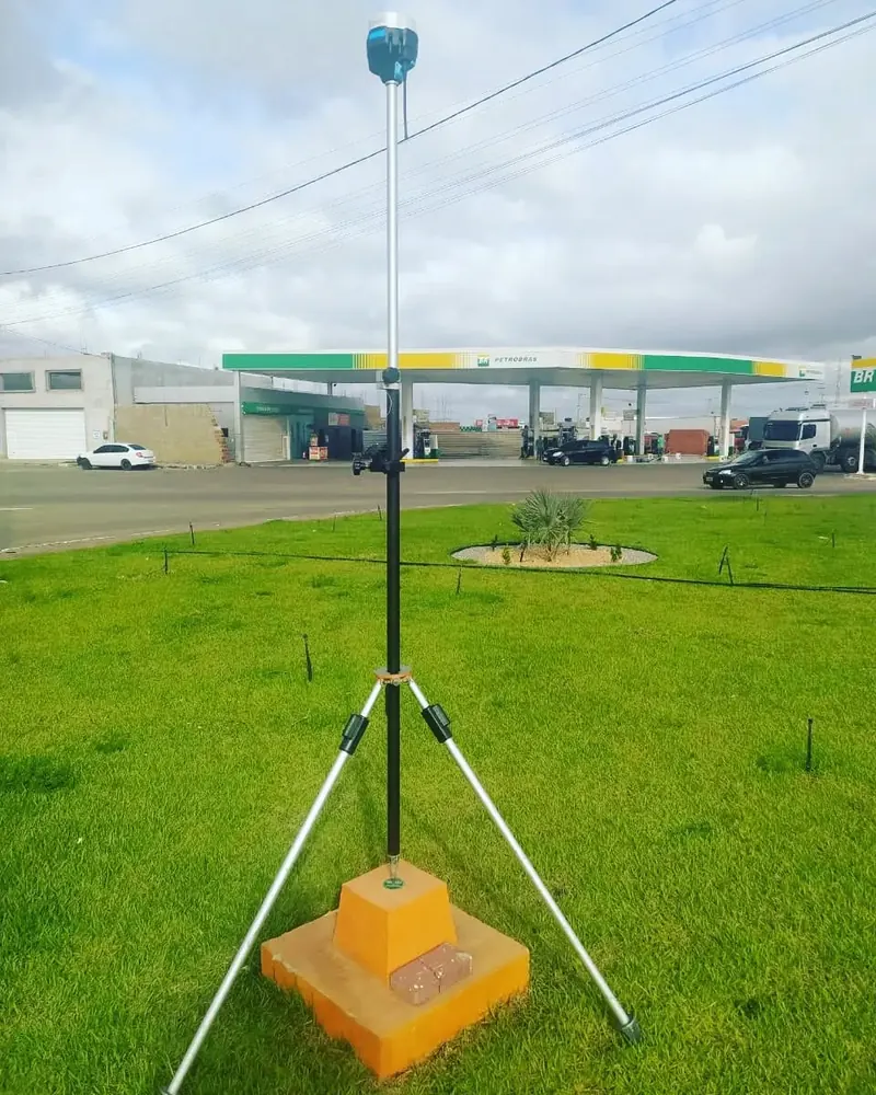 Receptor GNSS em tripé sobre um marco, em área gramada
