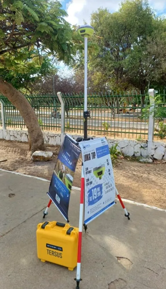 Receptor GNSS em exposição, com banner do Luka Tap e maleta Tersus